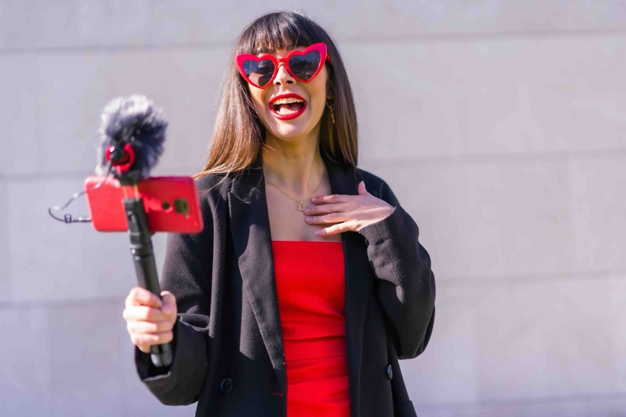 A creator in red heart-shaped sunglasses talking to camera on a handheld phone rig fitted with a microphone
